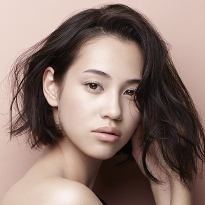 ベージュの背景でポーズする女性 レタッチ画像